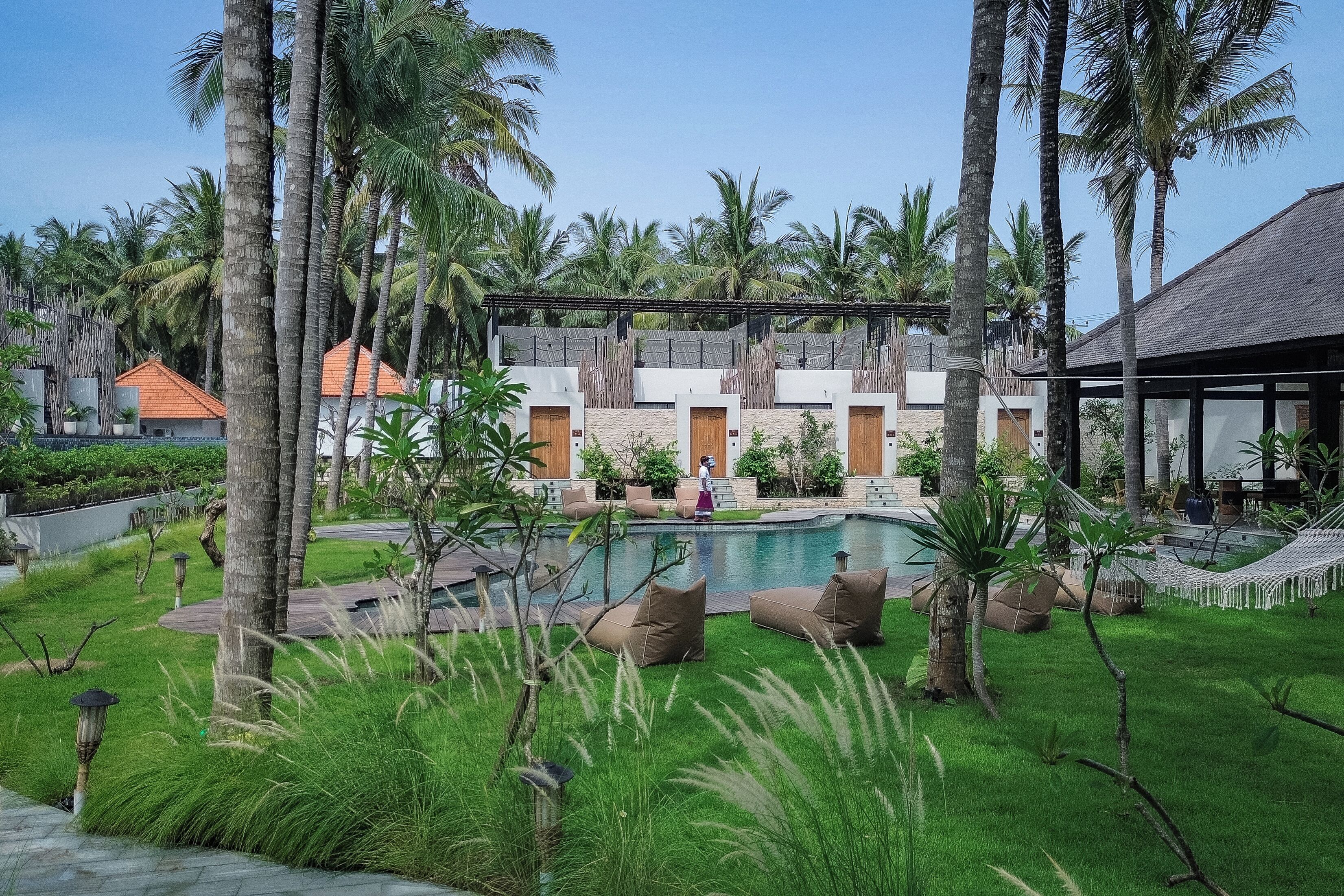 A resort with a swimming pool, palm trees, and a building with multiple rooms.