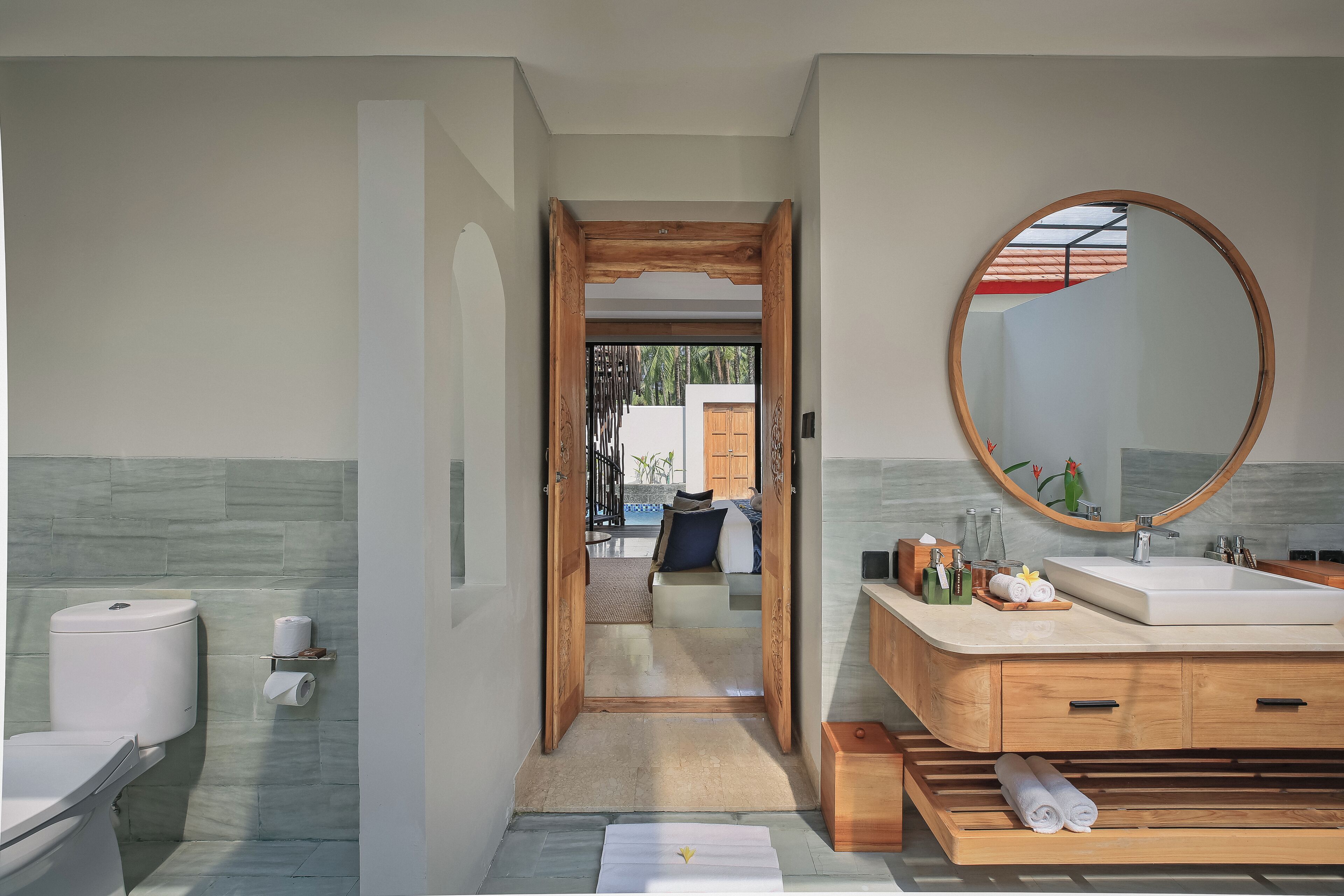 Une salle de bain moderne avec un meuble-lavabo en bois, un grand miroir et une vue sur une chambre.