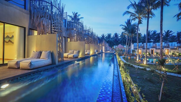 A poolside area with lounge chairs and a modern building with a unique bamboo-like facade. - The Sebali Penida Beach Resort (Penida Island)