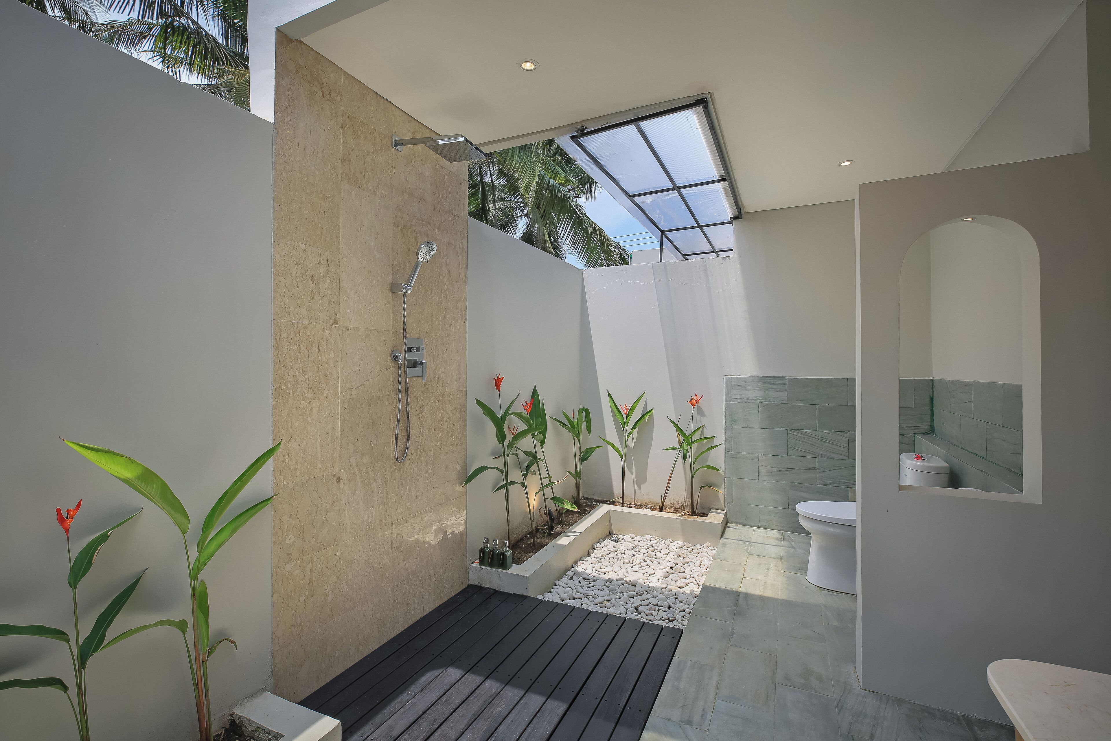 Une salle de bain moderne équipée d’une douche, de toilettes et d’un lavabo, avec une lucarne et des plantes en pot.
