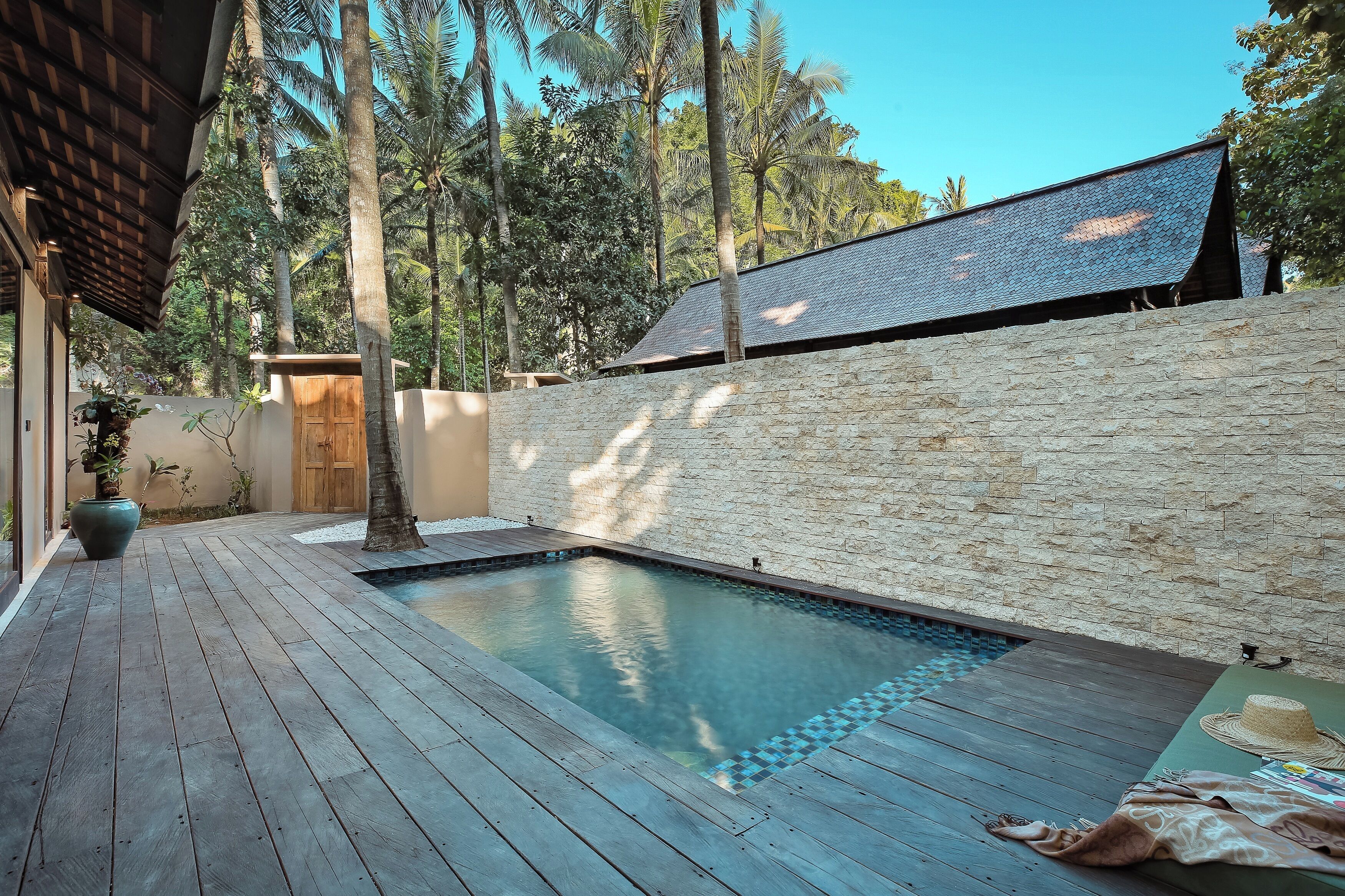 Une terrasse en bois avec une piscine, des murs en pierre et une porte en bois.