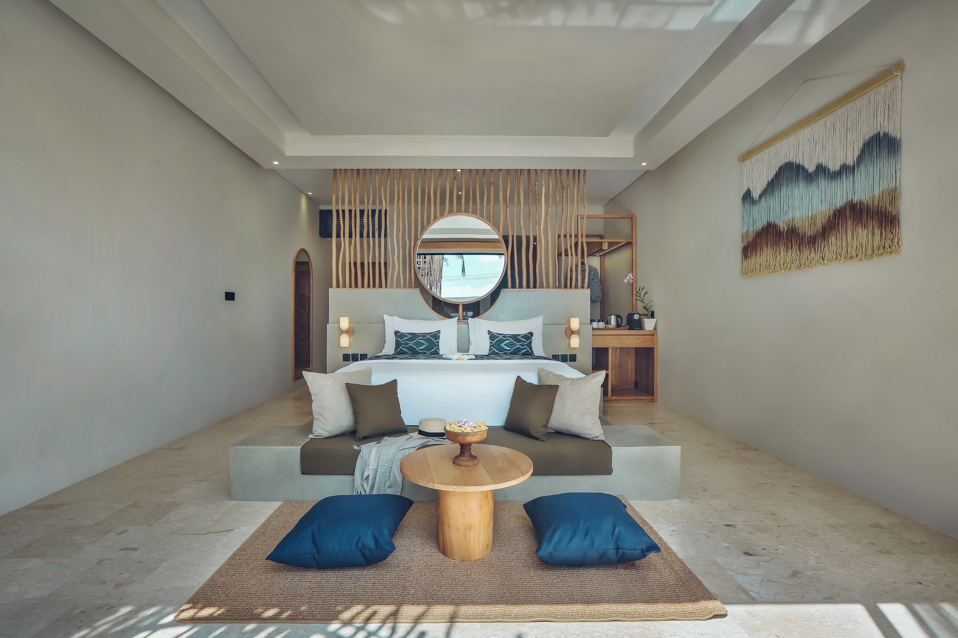 A modern bedroom with a large bed, a round wooden table, and a decorative wall piece.