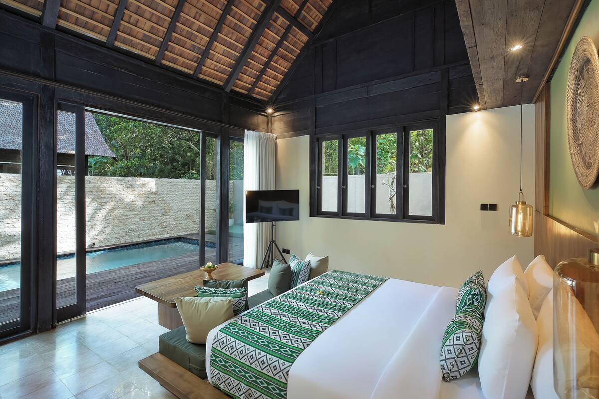 A bedroom with a large bed, a TV, a small table, and a view of a swimming pool.