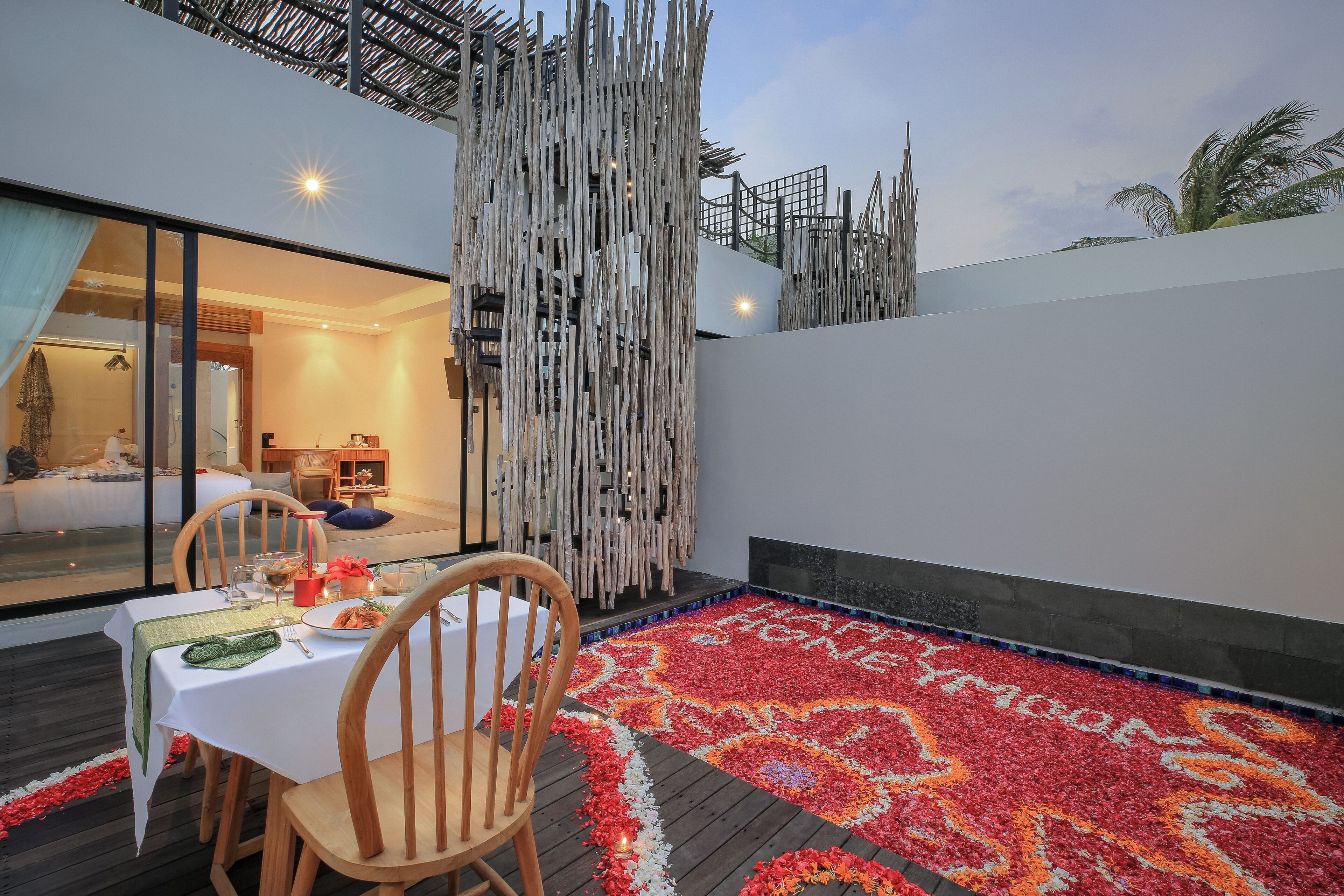 Un comedor con una mesa preparada para dos, un tapete decorativo y vistas de un dormitorio con cama y mesita de noche.