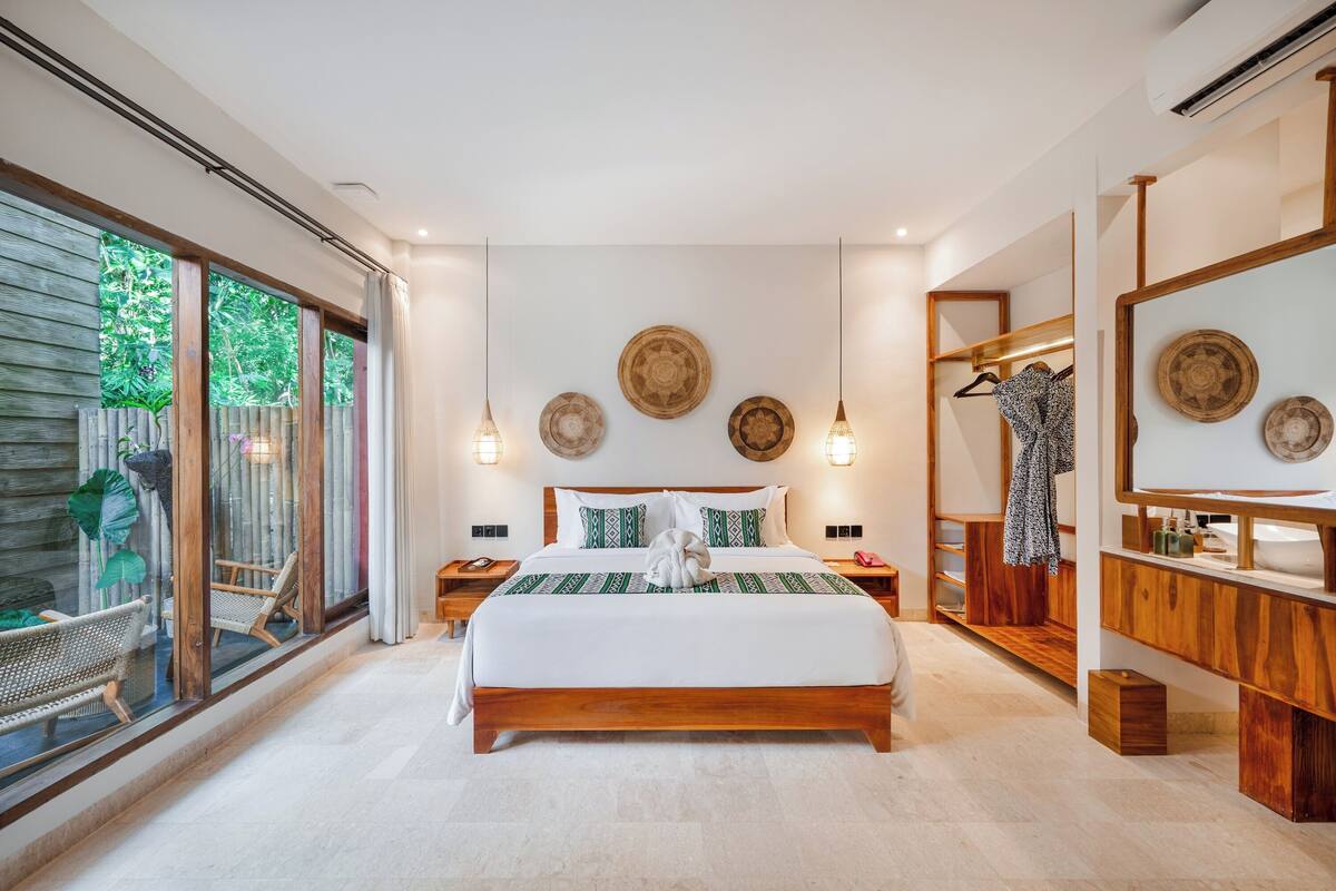 A spacious bedroom with a large bed, wooden headboard, and a view through a sliding glass door.
