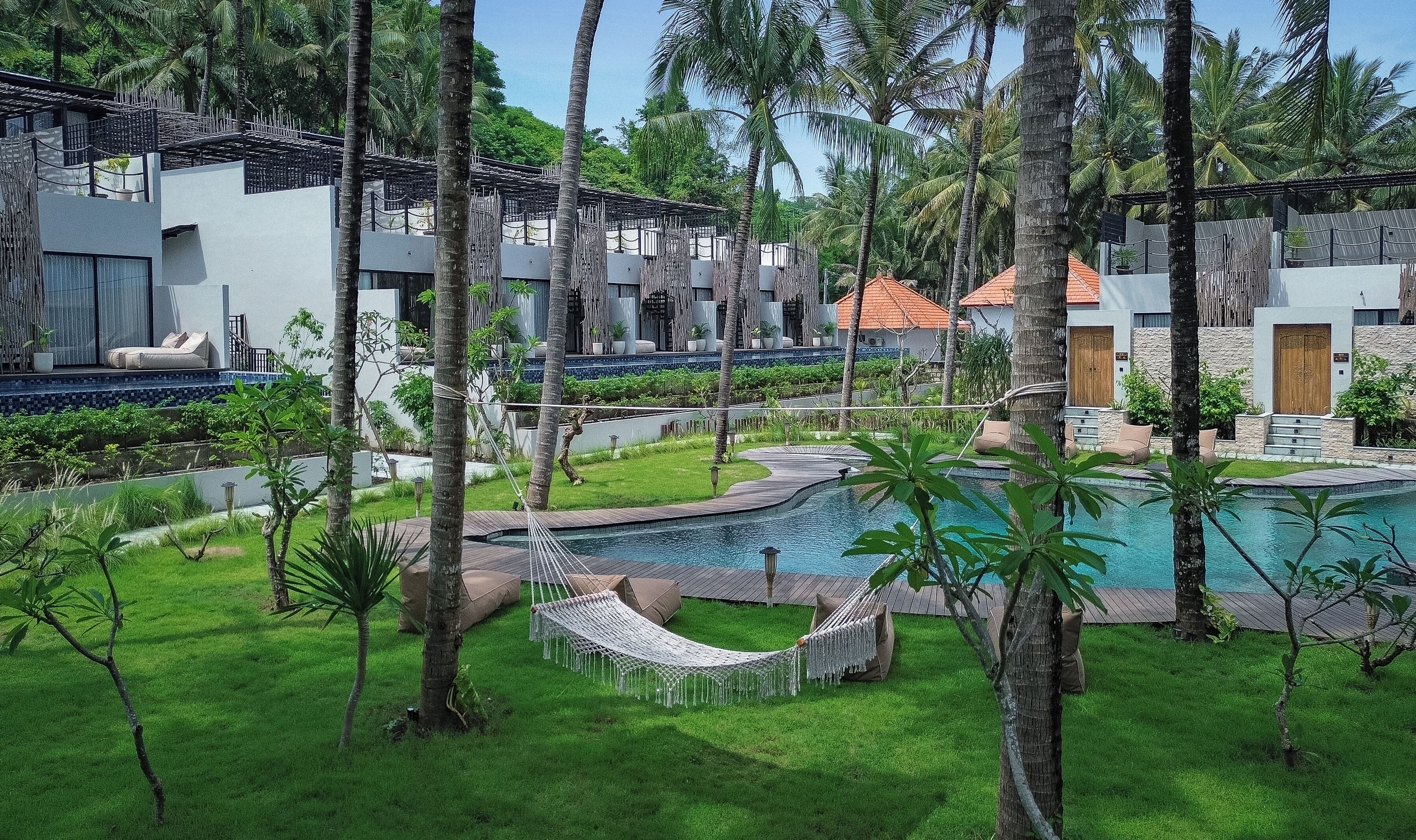 A resort with a swimming pool, hammock, and lush greenery.