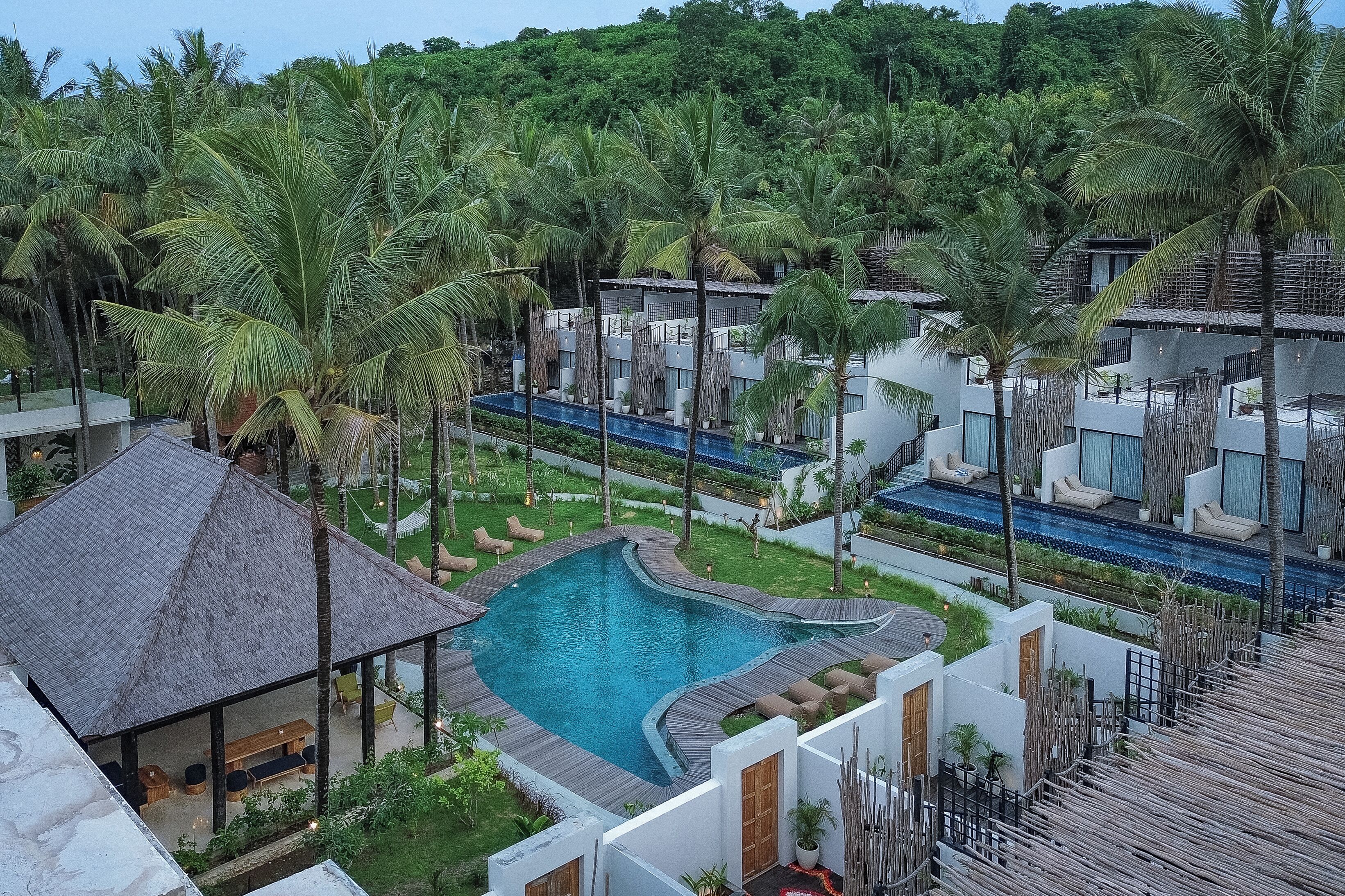 A resort with a central swimming pool, multiple guest villas, and lush greenery.
