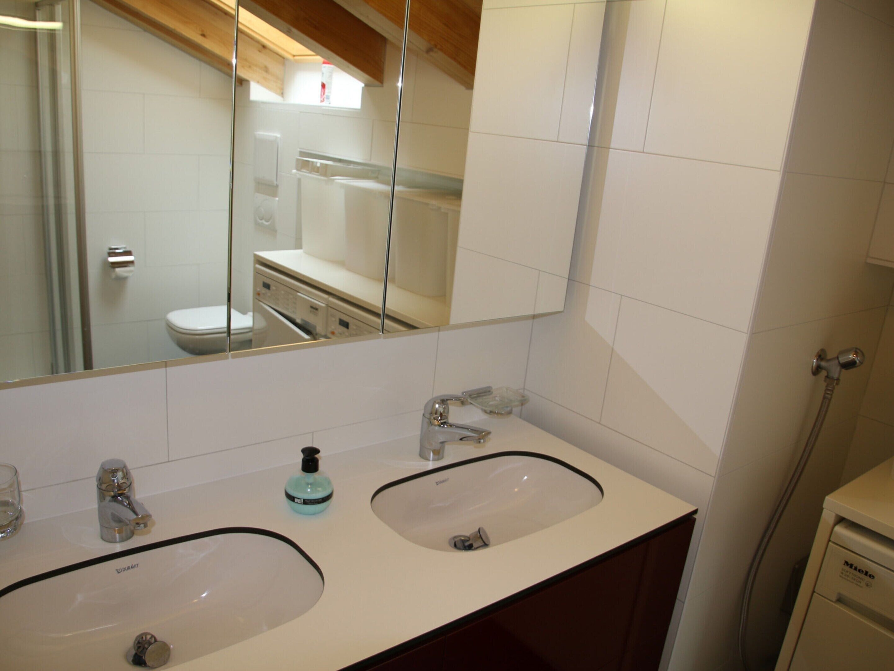 A bathroom with two sinks, a mirror, and a shower.