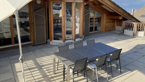 A wooden cabin with a covered patio, large sliding glass doors, and a table with chairs. - Hilltop Apartment With Valley Views (Veysonnaz)