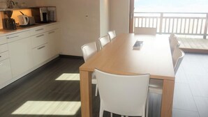 A modern kitchen with white cabinets and a wooden dining table. - Hilltop Apartment With Valley Views (Veysonnaz)