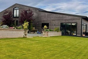 A modern house with a sloped roof, large windows, and a well-maintained lawn. - Large barn with hot-tub in the English countryside

 (Oakham)