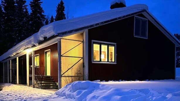 Een chalet met een ruime veranda, een schoorsteen en een raam met warme verlichting.