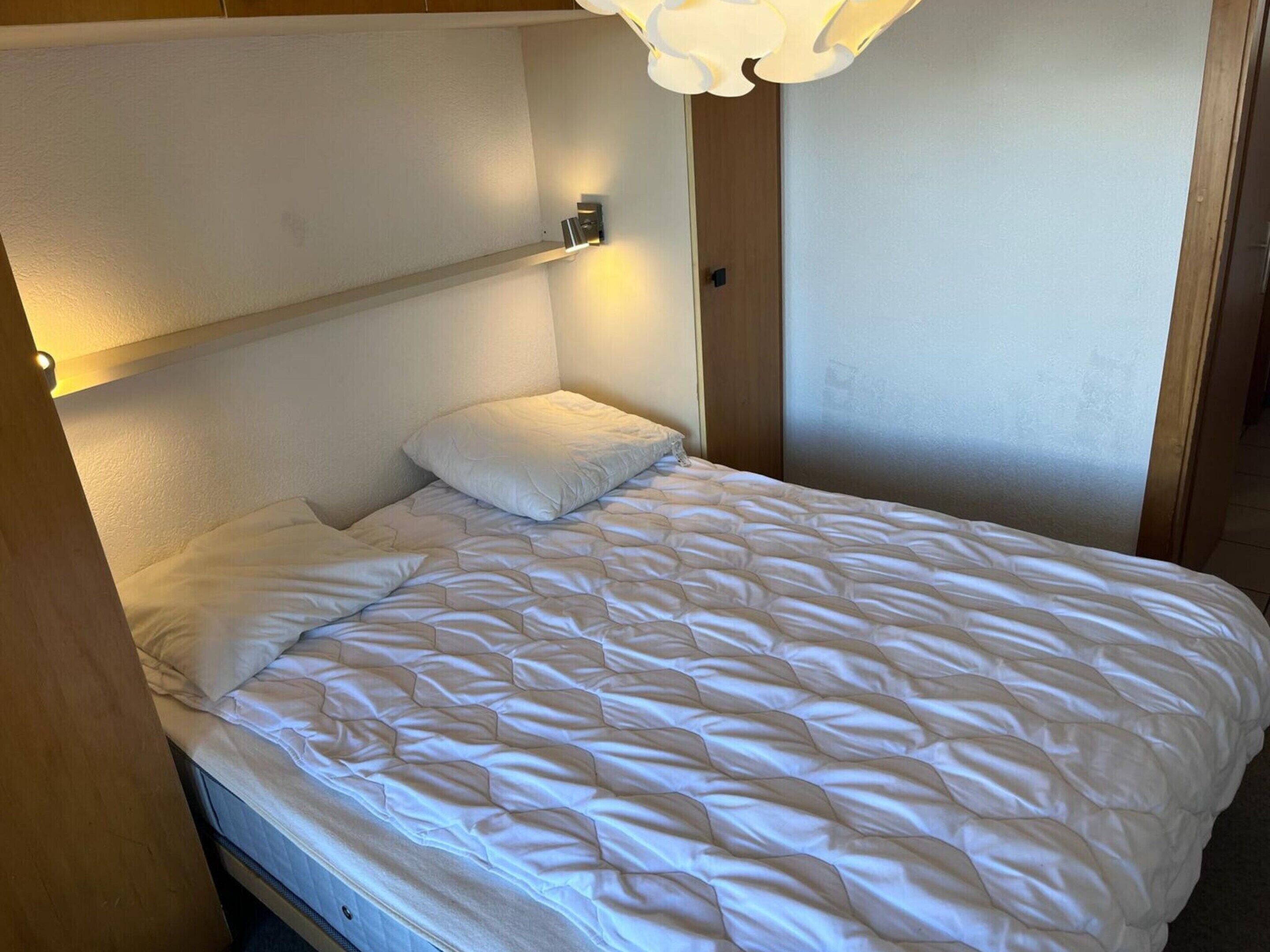 Un letto singolo con una coperta bianca, una lampada da comodino e una testiera in legno.