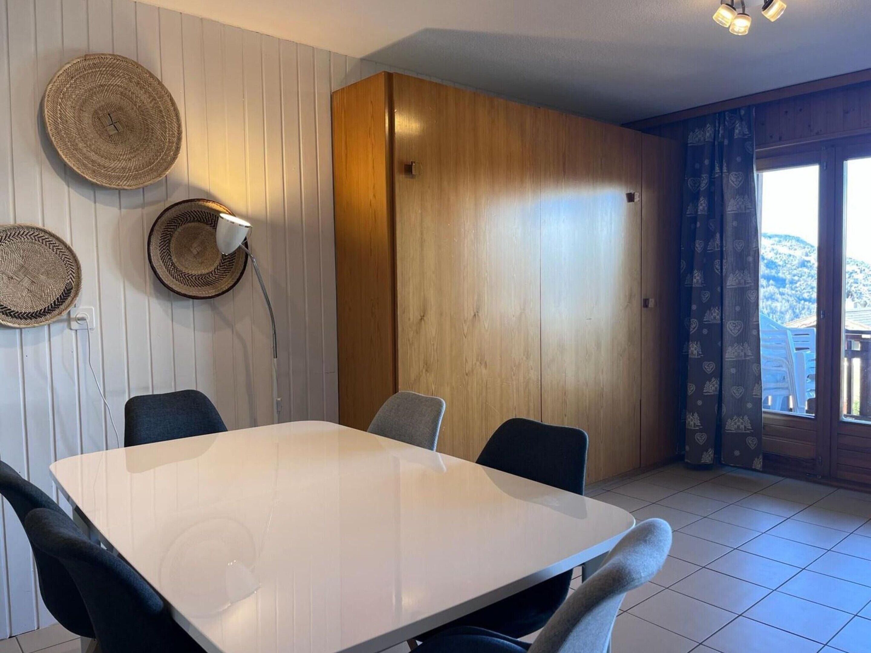 En matplats med ett vitt bord och fyra stolar, en vägglampa och vävda väggdekorationer.