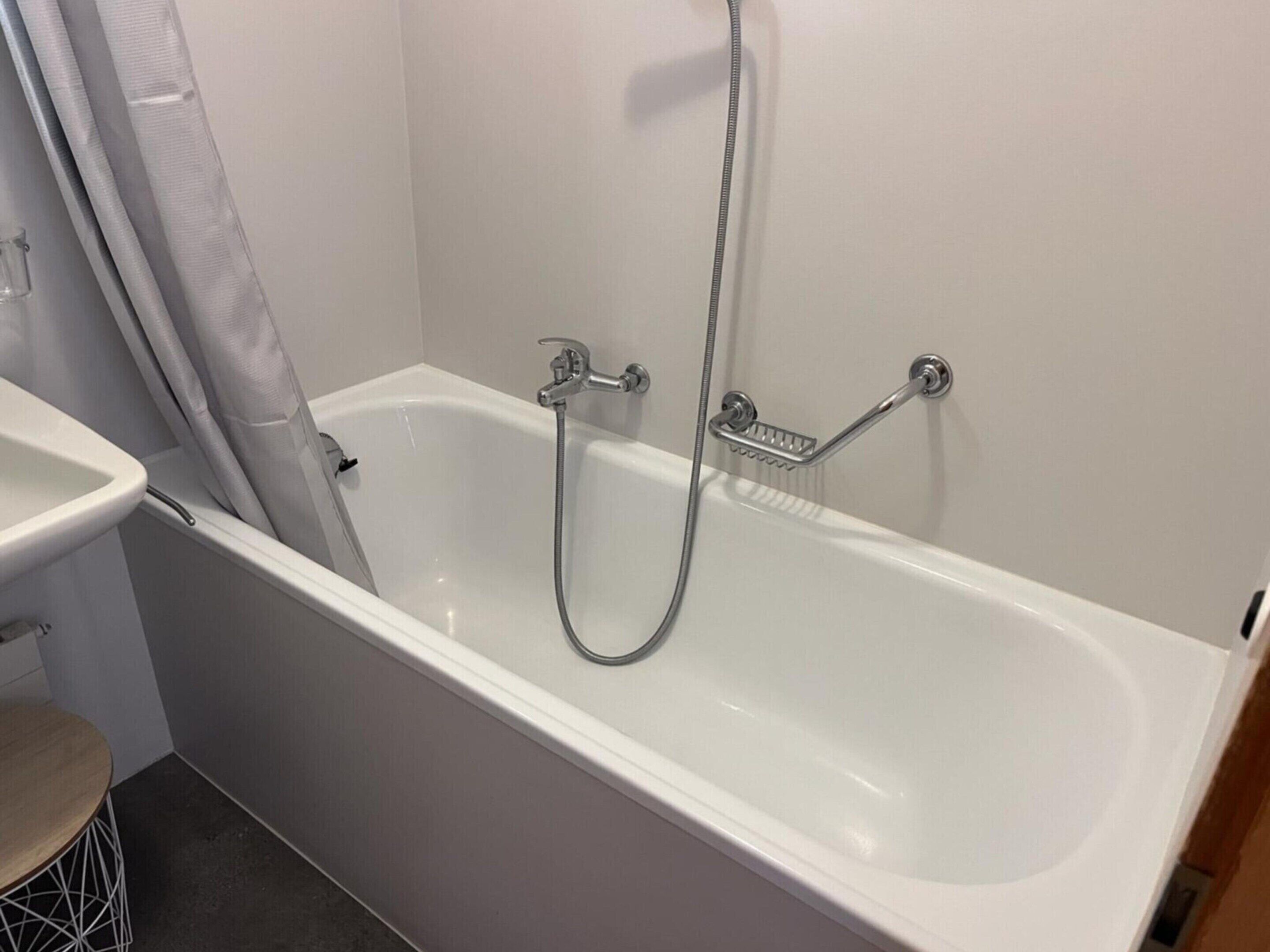 A white bathtub with a handheld showerhead and a grab bar.
