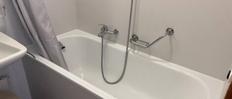 Eine weiße Badewanne mit Duschbrause und einer Haltestange.