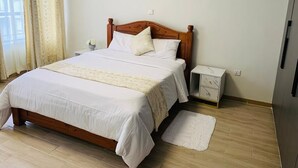 A bedroom with a wooden bed, white bedding, a bedside table with a lamp, and a small white rug on the floor.