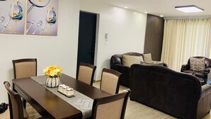 A modern living room with a dark brown sofa, a dining table with chairs, and a decorative vase with flowers.