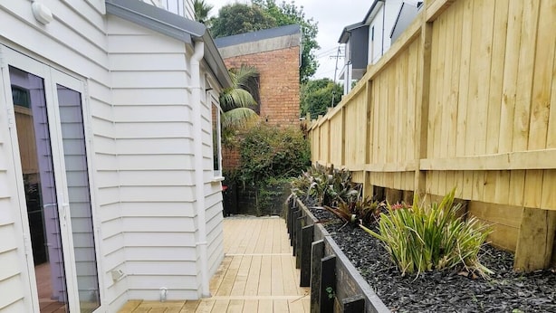 Une terrasse en bois, avec un mur de briques et une clôture en bois en arrière-plan.