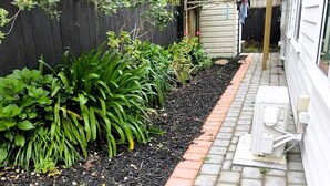 Un chemin de jardin recouvert de paillis, bordé de briques, qui mène à une structure en bois dotée d’un toit.
