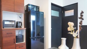 A compact kitchen with a black refrigerator, wooden cabinets, a coffee maker, and two white vases on the counter. - HARRISON (Sapporo)