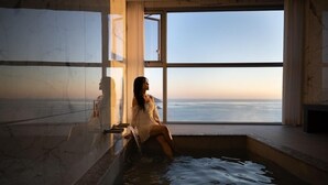 A person sitting by a window in a bathtub with a view of the sea.
