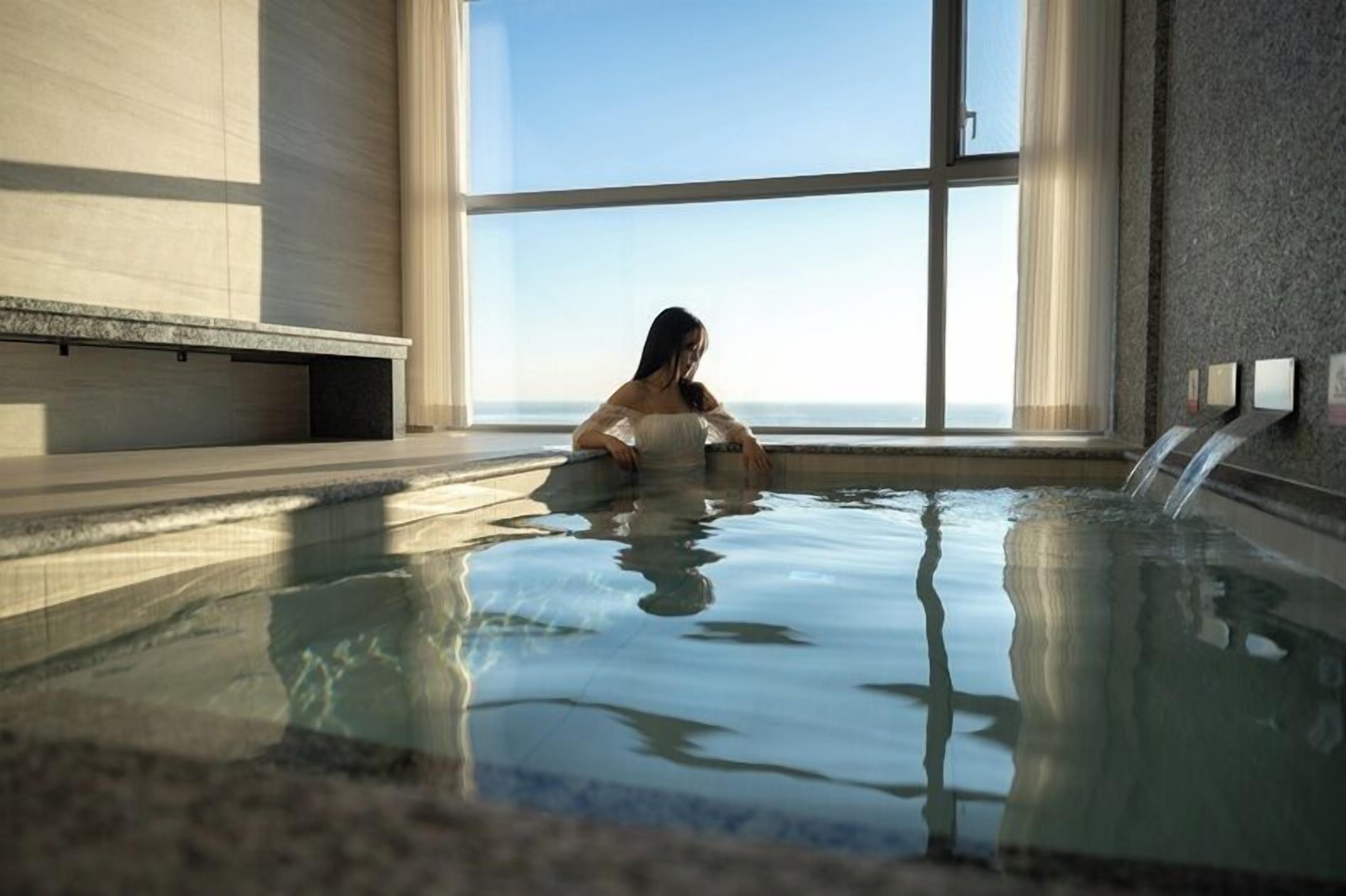 Eine Person in einem großen Innenpool mit Blick auf den Himmel durch hohe Fenster.