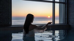 Ένα άτομο βρίσκεται σε ένα δωμάτιο με ένα μεγάλο παράθυρο που προσφέρει θέα σε μια μεγάλη έκταση νερού και σε ένα ηλιοβασίλεμα.