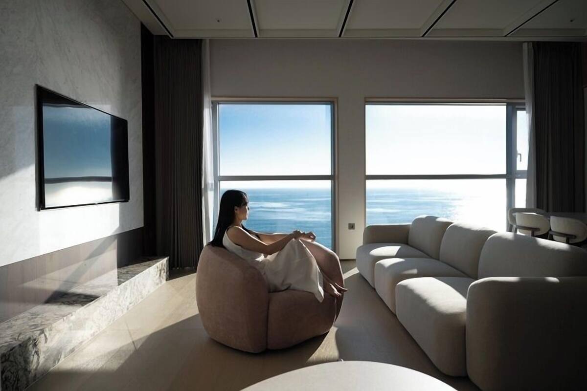 Un salon moderne doté d’une grande fenêtre donnant sur un plan d’eau, d’un canapé et d’un téléviseur à écran plat fixé au mur.