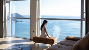 A modern living room with a large window offering a view of the sea and a distant island.