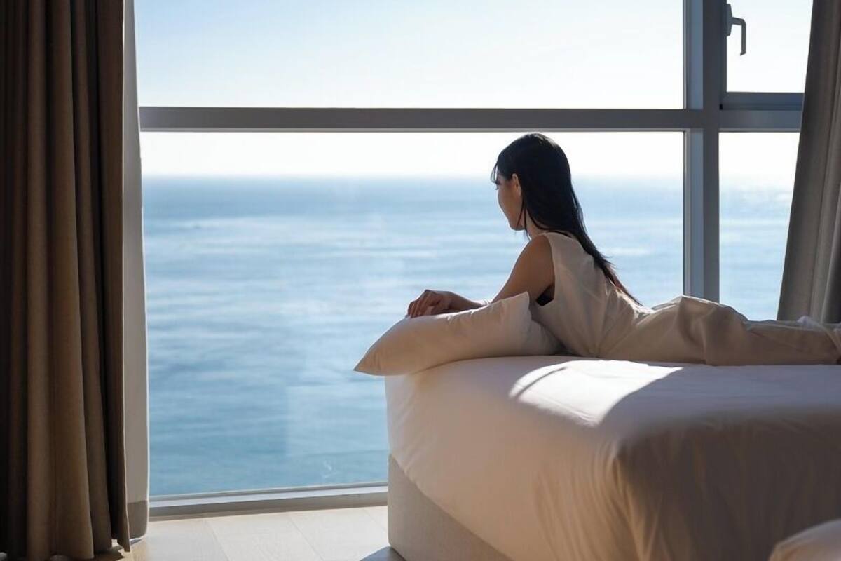 Une chambre avec une grande fenêtre donnant sur l’océan, un lit et une table de chevet.