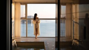 A room with a large window overlooking a body of water, a bathtub, and a view of the sea.