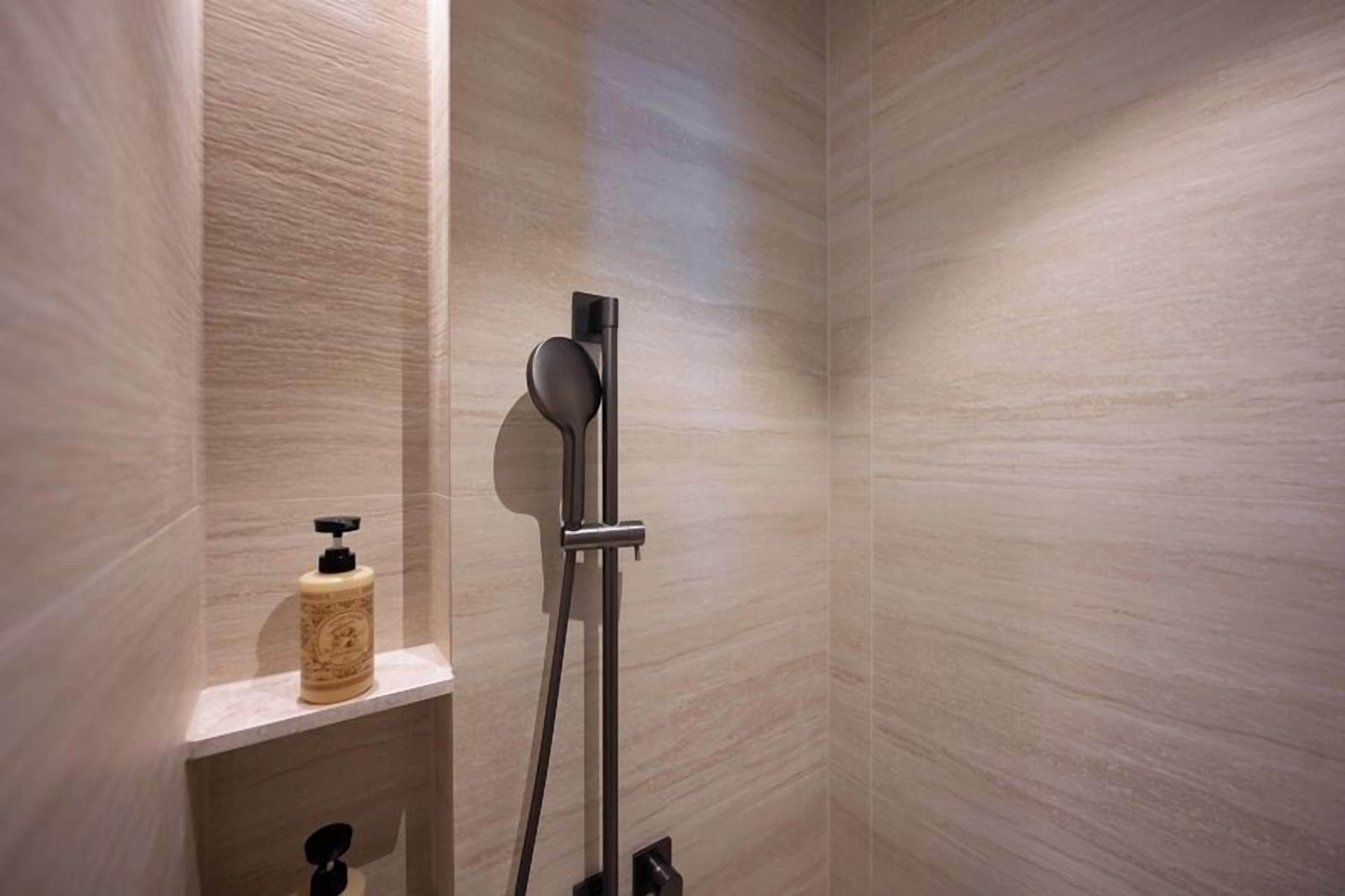 A modern bathroom with a shower, a soap dispenser on a shelf, and a towel rack.