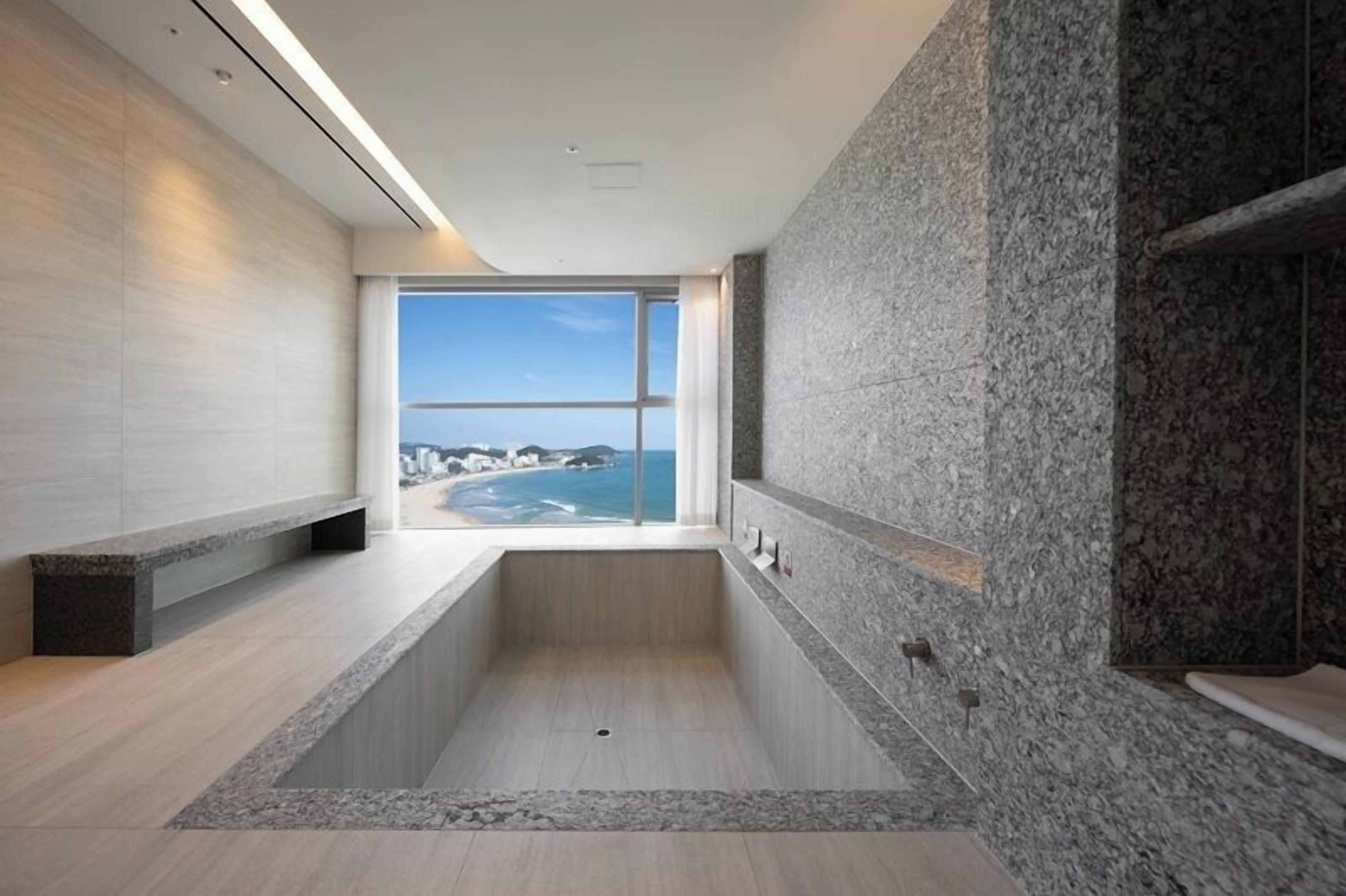 Une salle de bain moderne avec une grande baignoire, une vue sur l’océan et un mur en pierre.