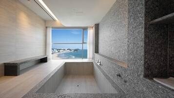 Une salle de bain moderne avec une grande baignoire, une vue sur l’océan et un mur en pierre.