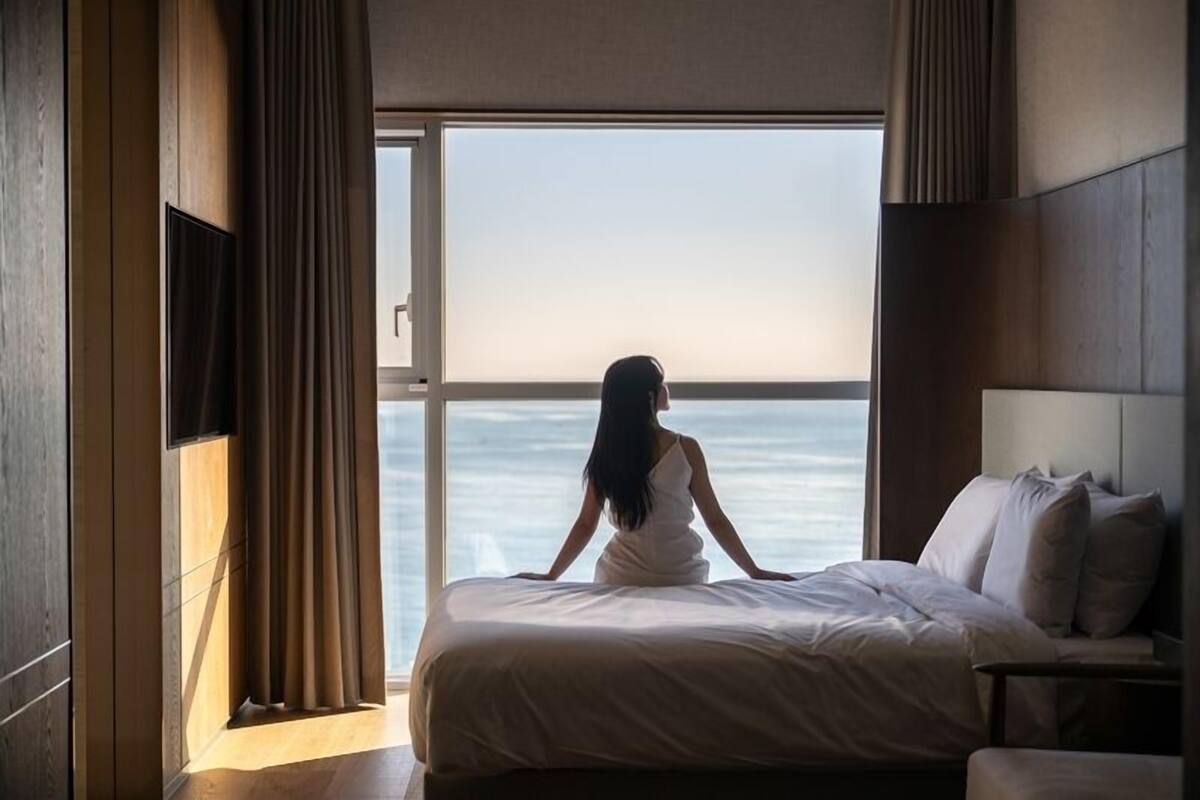 Une chambre avec une grande fenêtre, un lit et une table de chevet.