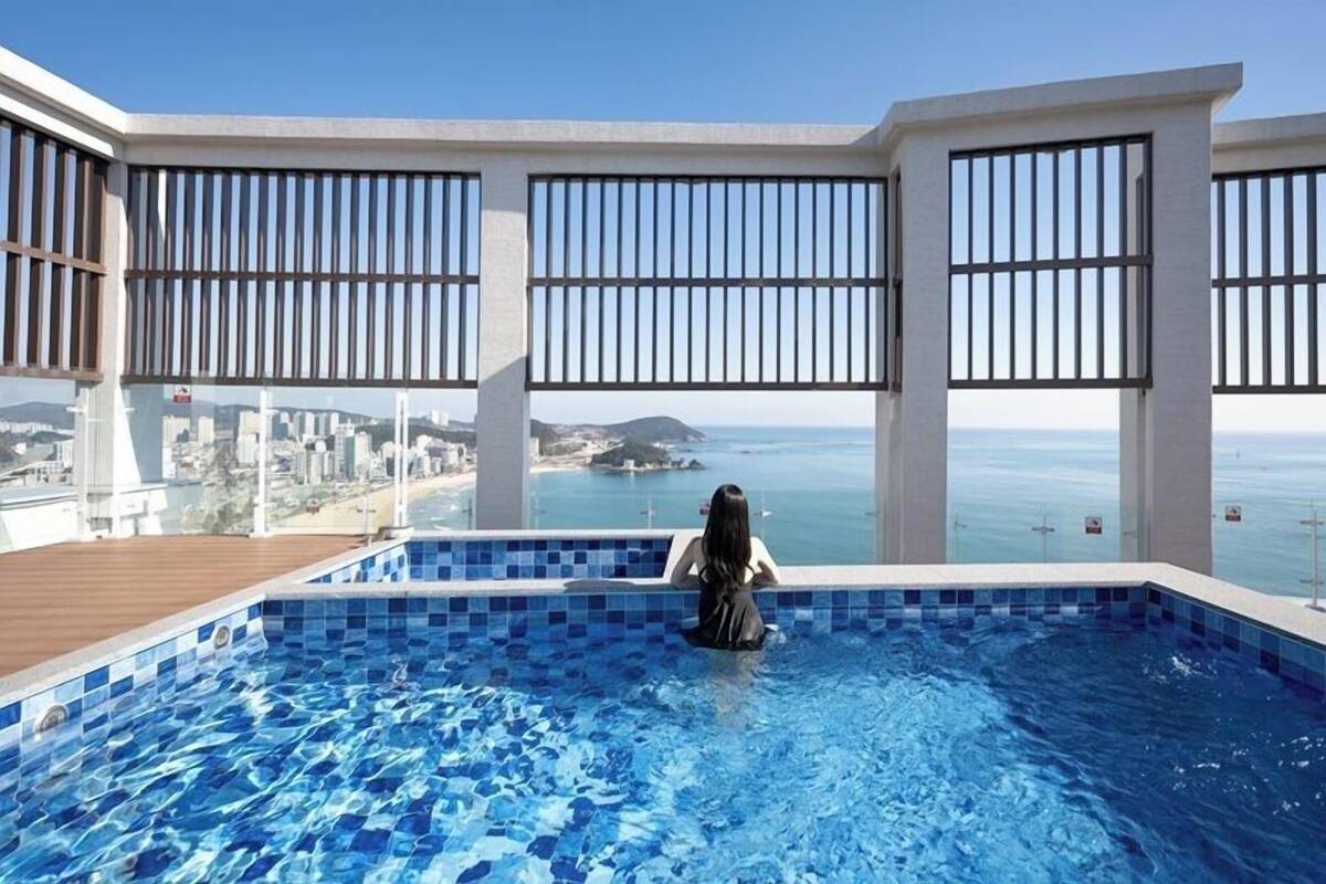 Une piscine avec vue sur la mer et le paysage urbain, de grandes fenêtres et une terrasse en bois.