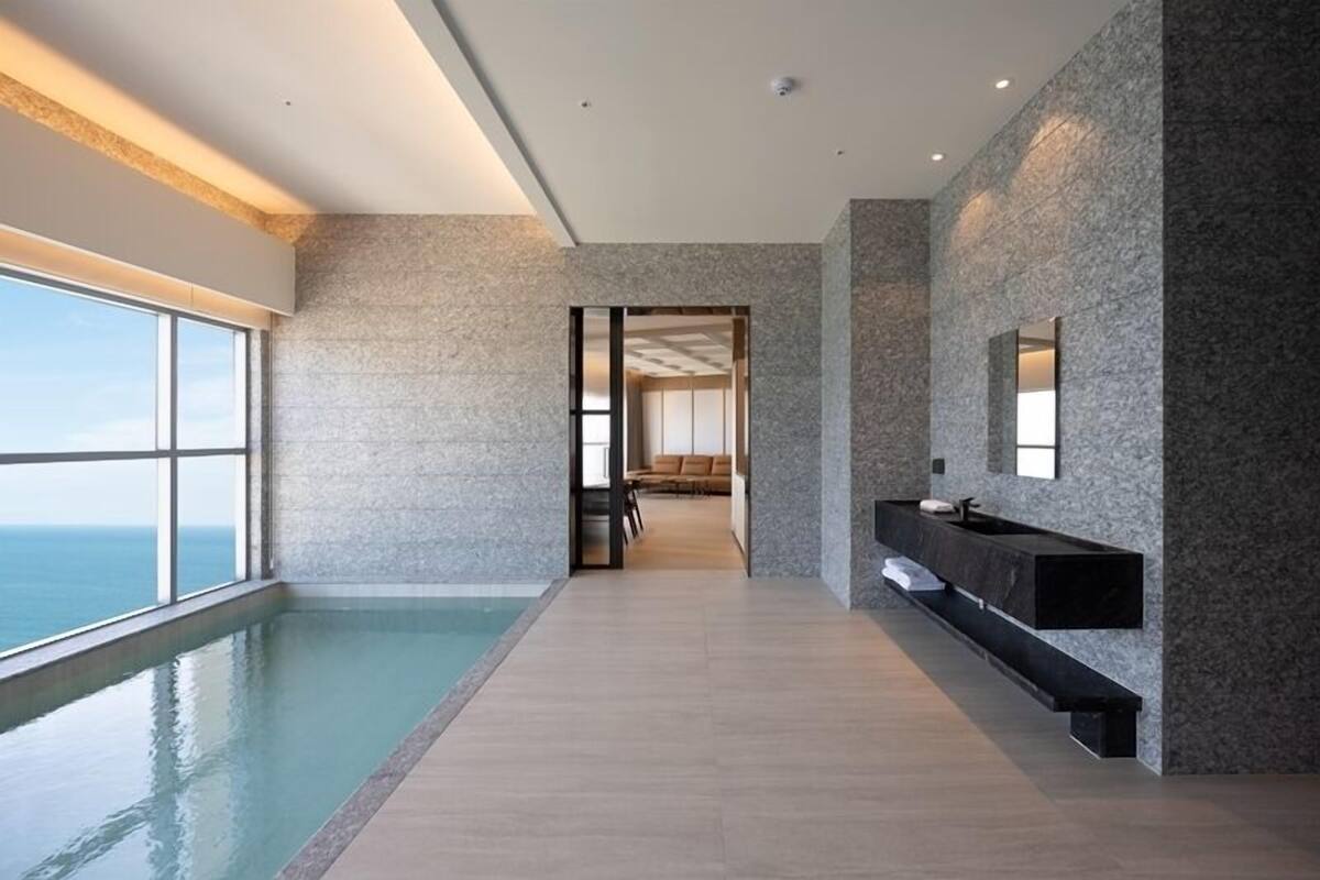 Une piscine à débordement moderne offrant une vue sur l’océan, une salle de bain minimaliste avec un lavabo et un miroir noirs, et un coin salon confortable avec un canapé et des fauteuils.