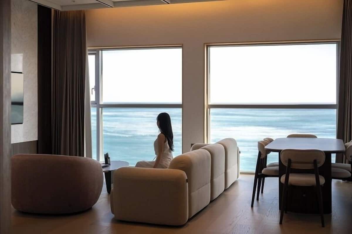 Un salon moderne avec une grande fenêtre donnant sur la mer, un canapé, une table à manger et un téléviseur.