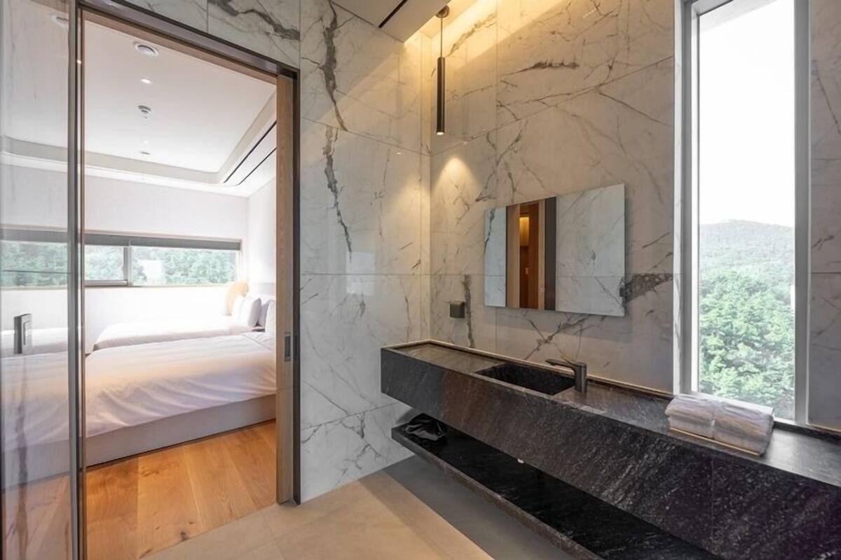 Une salle de bain moderne avec un mur en marbre, un grand miroir et un lavabo noir.