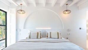 A modern bedroom with a large bed, two wall-mounted lamps, and a large window with a view of palm trees. - Impressive Farmhouse With Pool (Santa Eulalia del Rio)