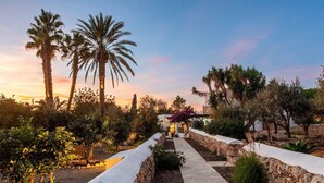 A stone pathway leading to a building with a white facade, surrounded by palm trees and various shrubs. - Impressive Farmhouse With Pool (Santa Eulalia del Rio)