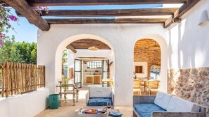 A cozy outdoor seating area with a stone wall, wooden furniture, and a view into the kitchen. - Impressive Farmhouse With Pool (Santa Eulalia del Rio)