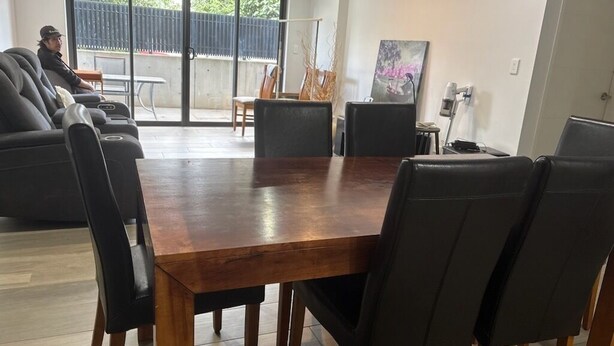 Un área de comedor moderna con una mesa de madera y sillas negras, un cuadro en la pared y vistas al exterior.