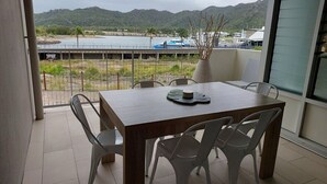 Un balcón con mesa y sillas, con vistas a un cuerpo de agua y colinas.