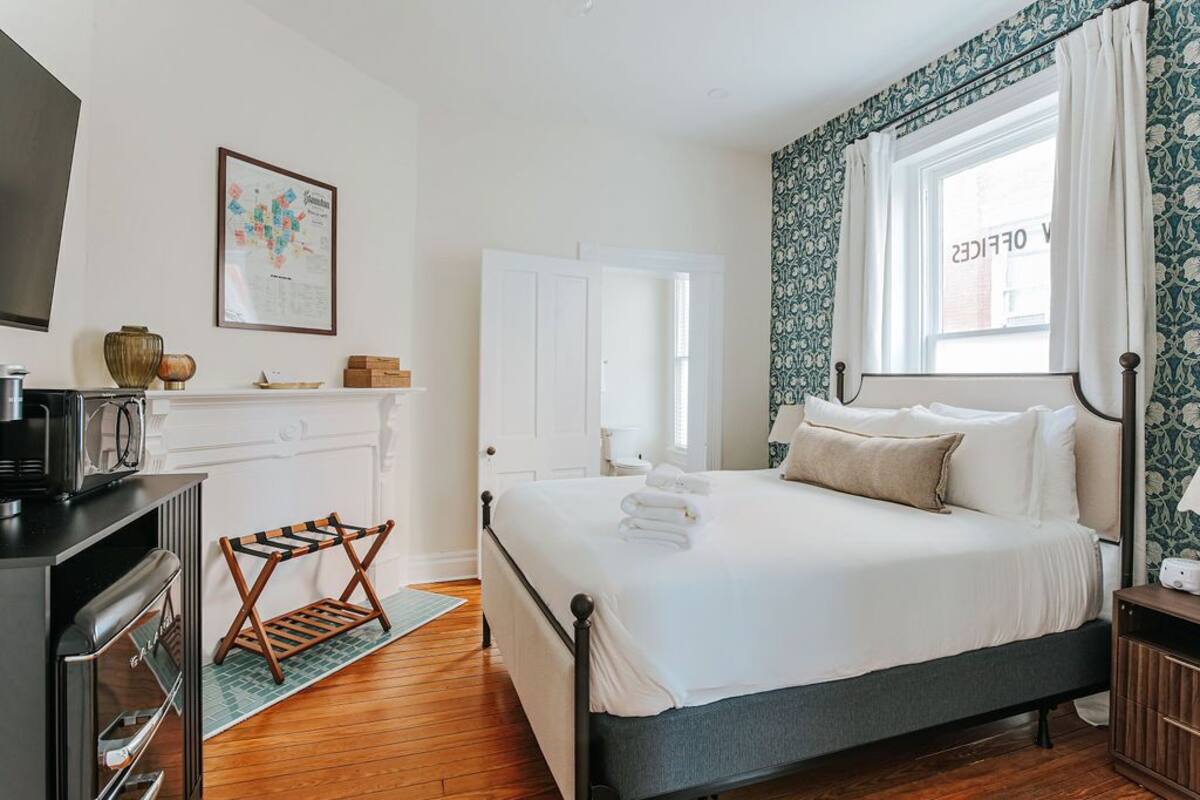 A bedroom with a bed, a dresser, a mirror, and a window with curtains.