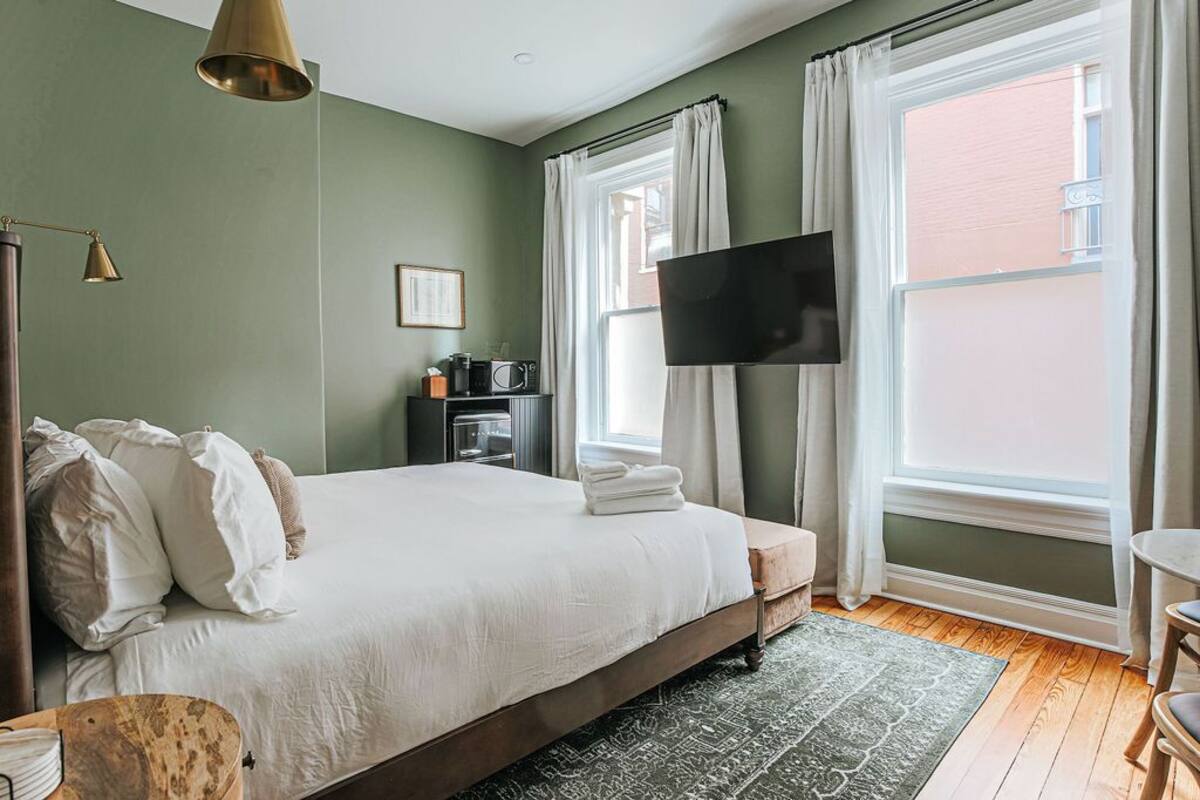 A bedroom with a bed, a TV, a bedside table, a chair, and a window with curtains.