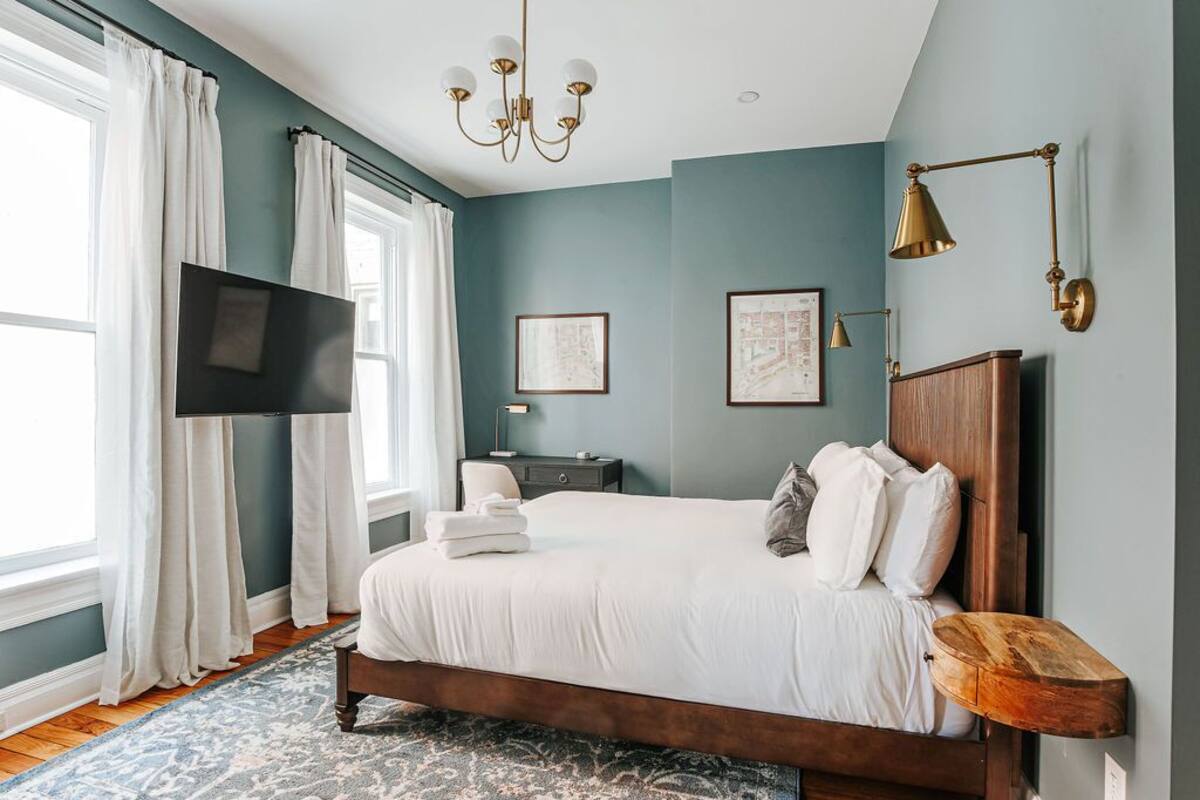 A bedroom with a large bed, a flat-screen TV, a wooden headboard, and a chandelier.