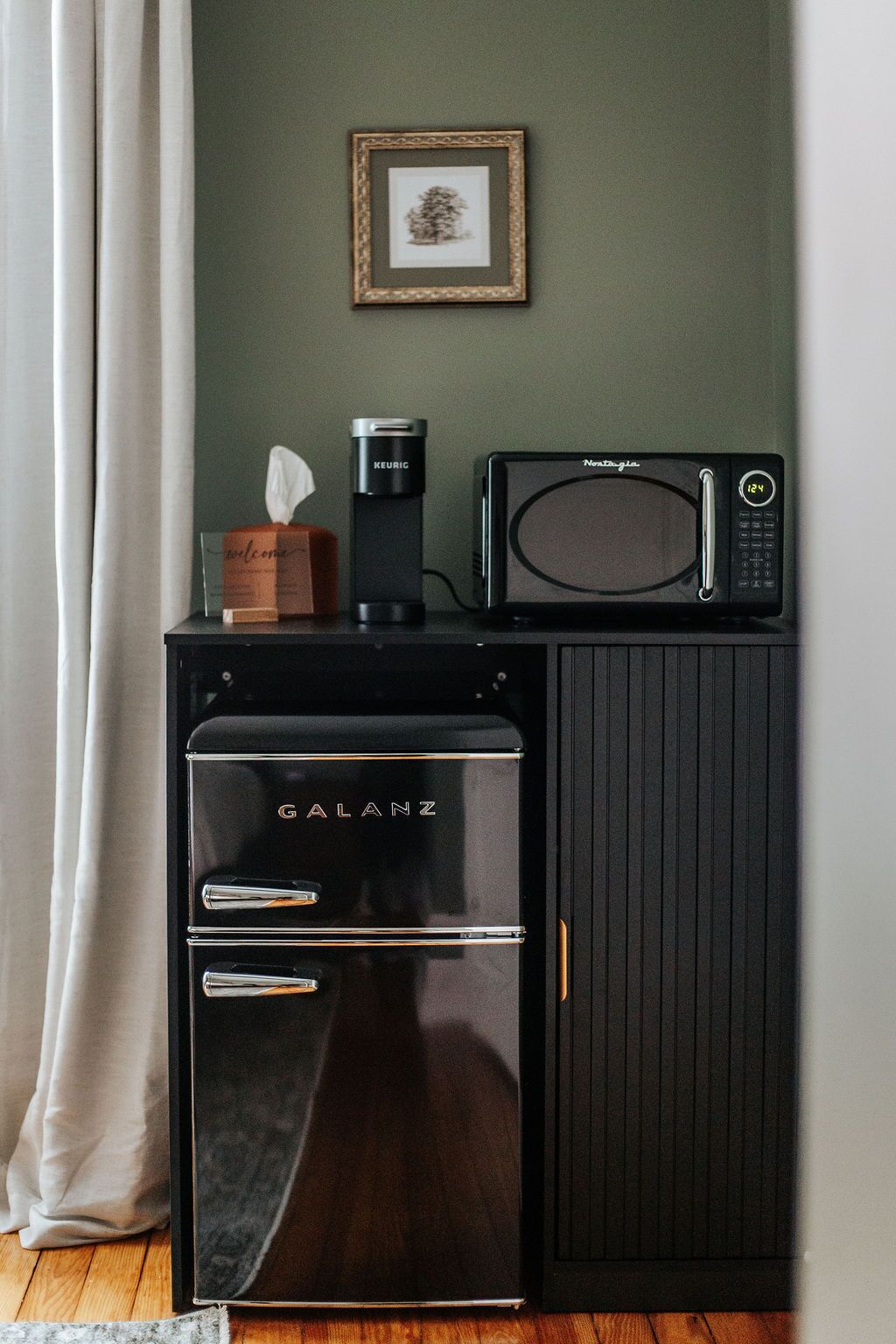 A compact kitchenette with a Galanz refrigerator, a coffee maker, and a microwave on a dark cabinet.