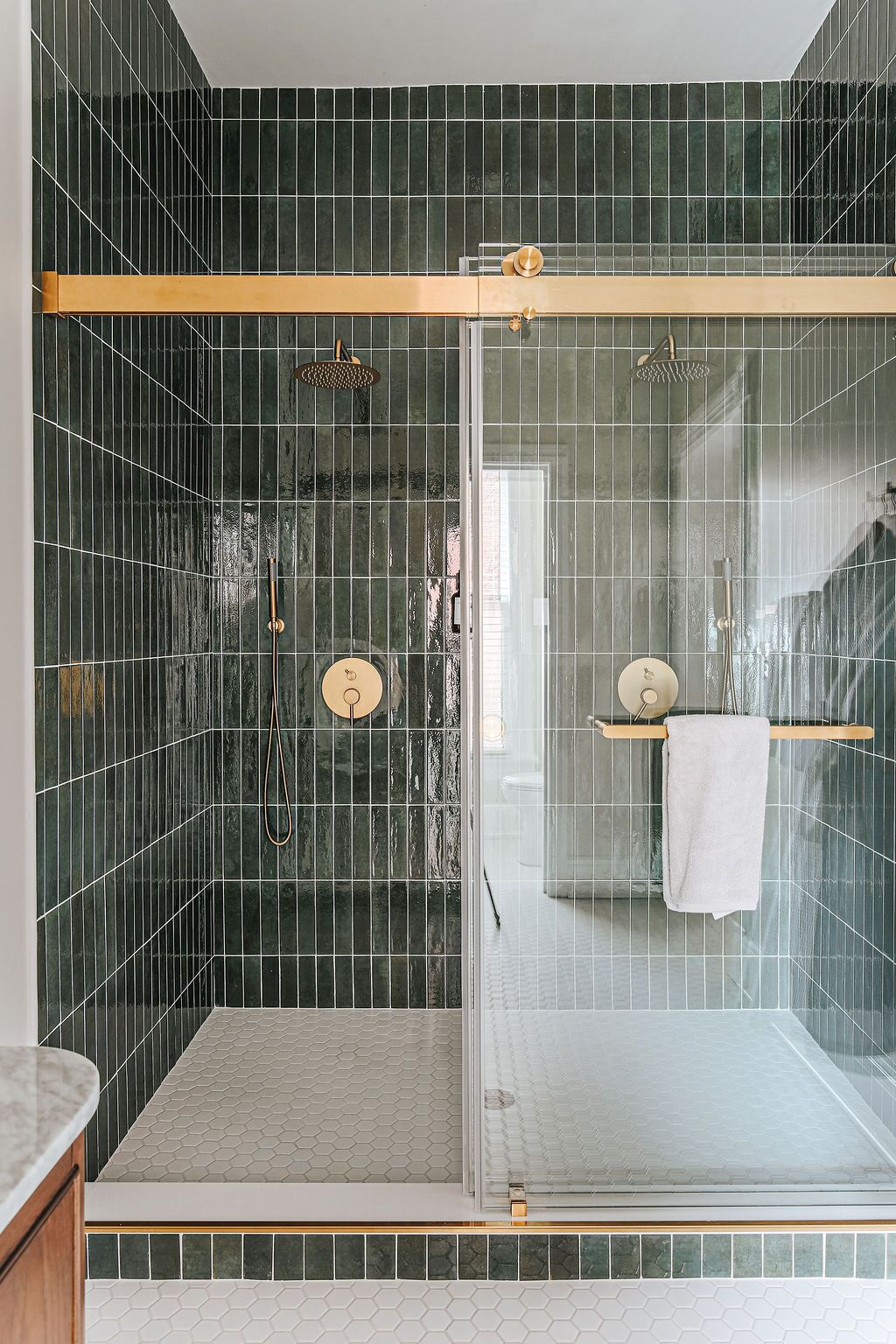 Un baño moderno con ducha envuelta en vidrio, paredes de azulejos verde oscuro y piso cubierto de azulejos blancos.